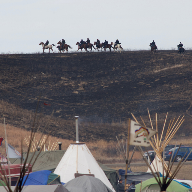 Young Native Americans on horseback make a defiant mid-day run up the hills, overlooking both the Oceti Sakowin Camp and the pipeline. The charred grass is from a fire in late October that threatened the camp. Protesters claim it was started by pipeline employees, but no arrests were ever made. 